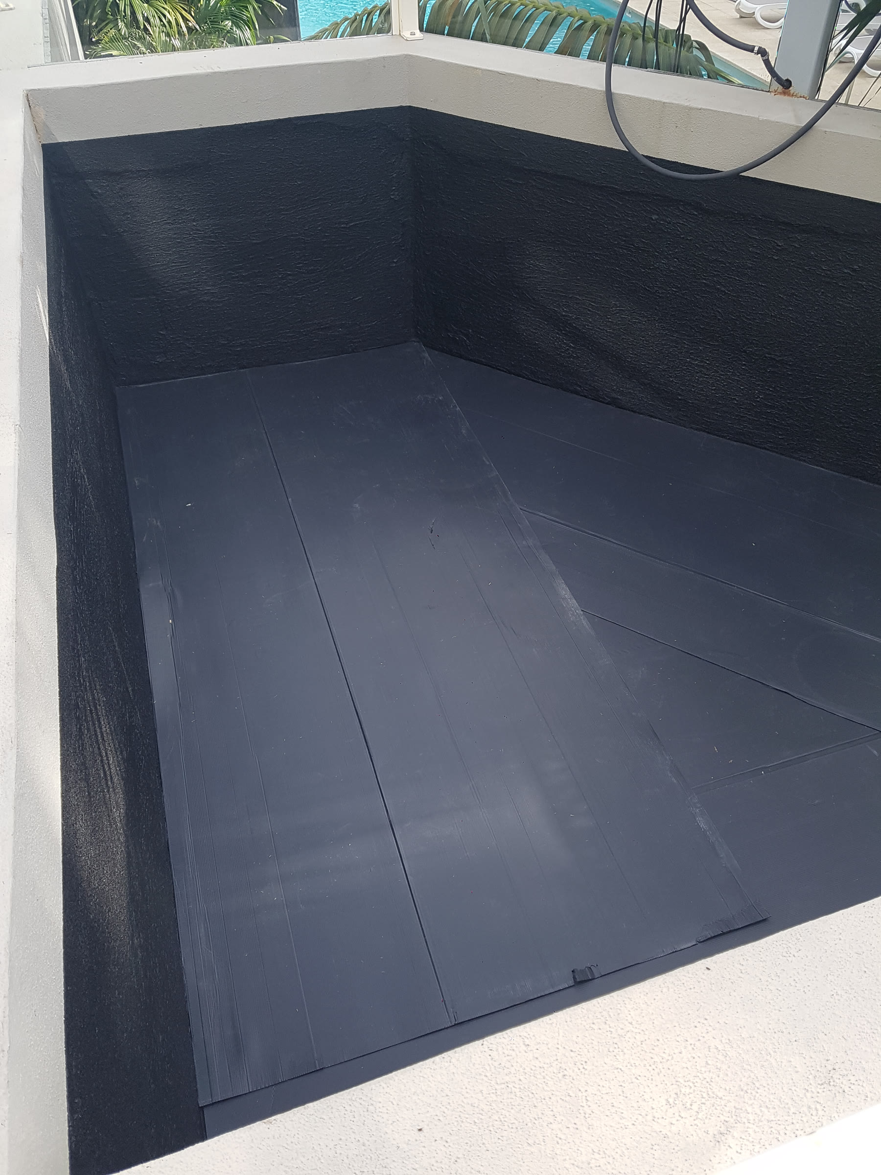Angular planter box lined with black waterproofing membrane by the pool